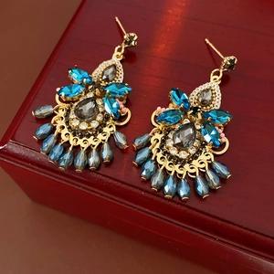 Luxurious gold-tone drop earrings with blue and gray faceted crystals on a dark wood box
