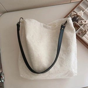 Detail of floral embroidery on beige cotton tote with black leather strap and metal clasp