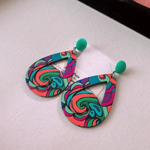 Detail of tear-drop acrylic earrings with colorful swirl patterns on beige fabric