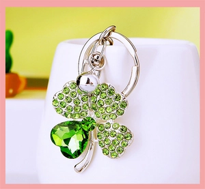 Close-up of silver four-leaf clover keychain with green crystals and a small bell