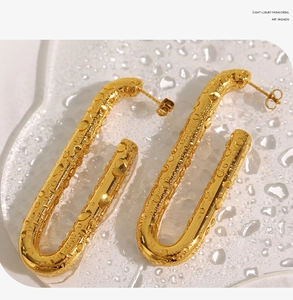 Makroaufnahme goldener U-förmiger Titanstahl-Ohrringe vor Wassertropfen-Hintergrund