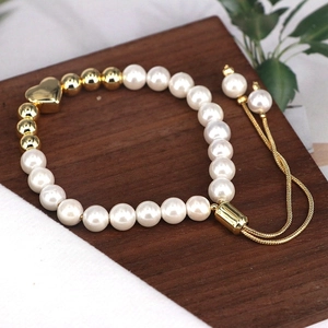 Detail of adjustable pearl bracelet with golden heart charm on dark wooden tray