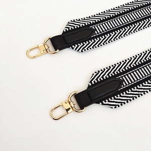 Detail of black and white herringbone weave strap with gold clips and leather trim