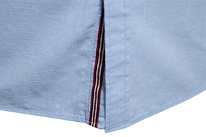 Détail de l'ourlet de chemise en lin bleu clair avec ruban rayé rouge blanc et noir