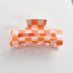 Detailed view of an orange and white checkered pattern hair claw clip on white background