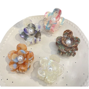 Five elegant acetate flower hair claws with pearls on a white plate, pastel colors