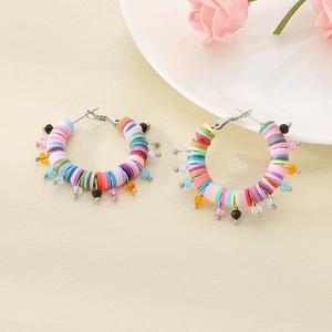 Detail of colorful polymer clay hoop earrings with small bead pendants on a textured surface