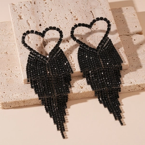 Macro shot of dark heart tassel earrings with black rhinestones on a travertine stone