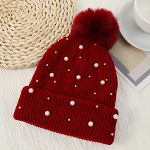 Detail of red ribbed knit beanie featuring pearls, beads, and a large fluffy pom-pom