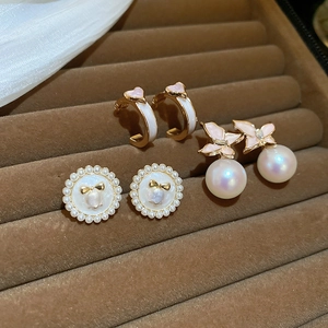 Détail de trois paires de boucles d'oreilles dorées avec fleurs roses et perles