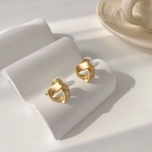 Detail shot of golden twisted geometric clip-on earrings on a white wavy stand