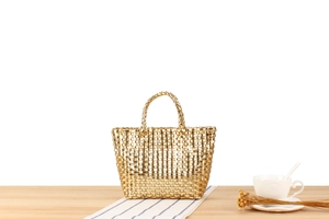 Détail d'un sac à main tissé doré métallisé avec double poignée et finition champagne