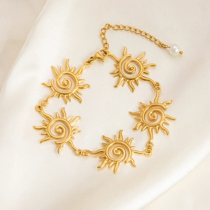 Detail of gold sun link bracelet with spiral patterns and small pearl charm on white silk