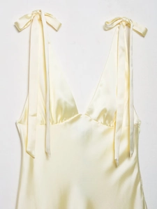 Detail of light yellow satin midi dress featuring elegant bow-tie shoulder straps