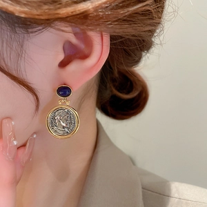 Close-up of vintage geometric coin earrings with blue gems worn by a female model