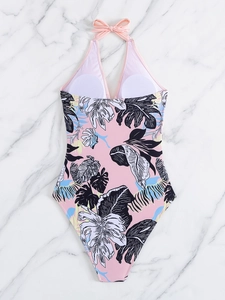 Flat lay of pink halter neck swimsuit with tropical leaf patterns on marble background