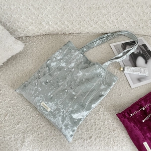 Detailed view of grey velvet tote bag with pearl accents on a soft white texture