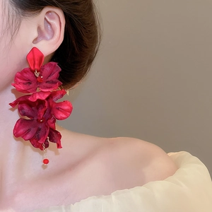 Detailed view of large red fabric flower earrings with elegant pearl fringe on model