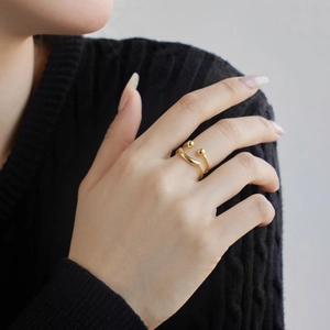 Close-up of golden wave ring with bead accents worn on finger with black knit sweater