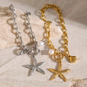 Detail of 18k gold and silver starfish bracelets with pearl and shell charms on a rock