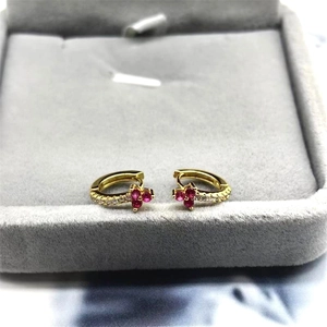 Macro detail of gold huggie earrings with ruby-red flower and white zircon accents