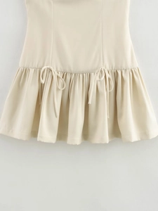 Detail of beige sleeveless dress showing drawstring bow and ruffled hem stitching