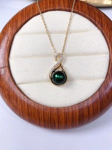 Close-up of a gold S-shaped pendant with diamonds and a dark green pearl in a box