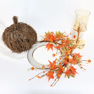 Close-up of autumn maple leaf garland with pumpkins and amber glass candle holder
