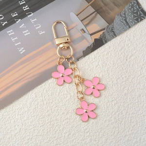 Golden keychain with three pink flower pendants on a textured beige background