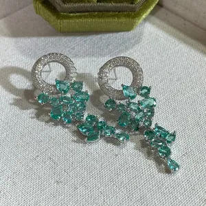 Détail de boucles d'oreilles émeraude en forme de poire avec zircons sur tissu blanc