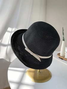 Detail of black straw cloche hat with white bow on elegant gold display stand