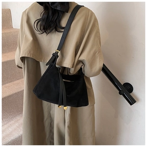 Detail of a black suede shoulder bag with gold hardware and side tassel zipper on a trench coat