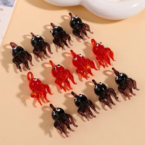 Top view of red and black glass octopus charms with loops on a minimalist beige background