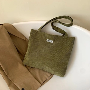 Close-up of green corduroy tote bag with Fashion Instinct label against beige blazer