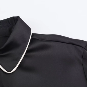 Detail of black satin shirt featuring contrast white piping and premium neck stitching