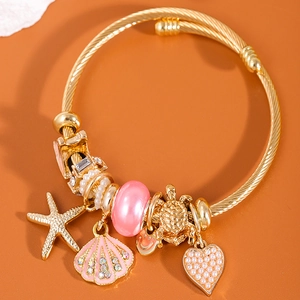 Golden open bangle with starfish shell and heart charms on a warm orange background