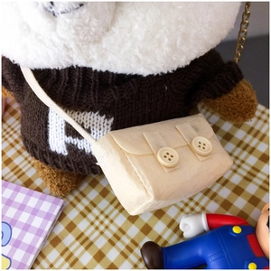 Detail of a beige felt crossbody bag accessory with decorative buttons on a plush bear