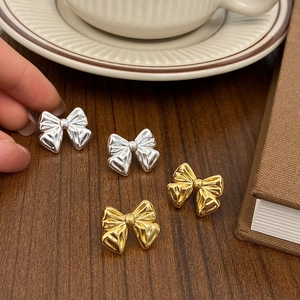 Minimalist bow-knot stud earrings in silver and gold finishes on a wooden surface