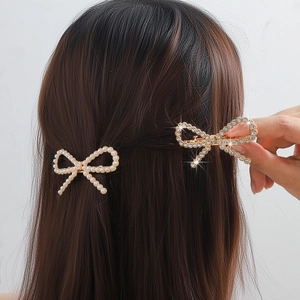 Detail showing elegant gold bow hair clips with pearls and rhinestones worn by a model