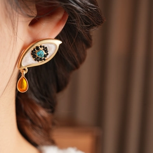 Macro view of vintage eye-shaped earring with heart-shaped teal stone and amber drop pendant