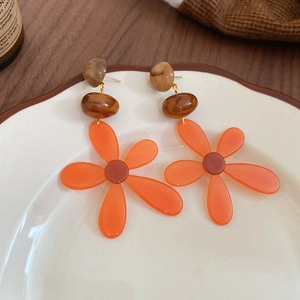Detailed view of resin floral tassel earrings with amber texture beads on a ceramic plate