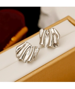 Detailed close-up of silver wavy earrings with fluid geometric folds on a textured box