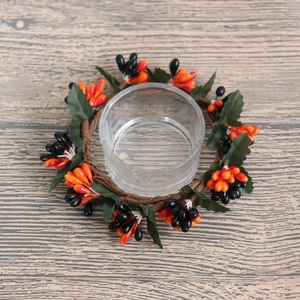 Halloween candle ring with black and orange berries, green leaves and glass cup on wood