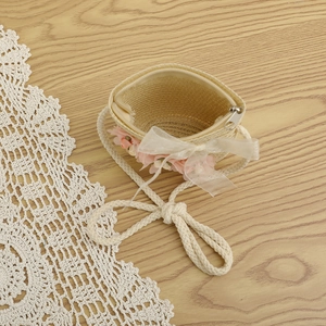 Détail du sac bandoulière en paille avec fleurs et dentelle sur fond de bois