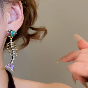Detail of fish bone pendant earring with green enamel and pearls worn by a model