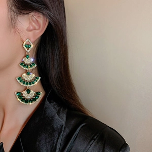 Detail of fan-shaped drop earrings with green rhinestones on elegant female model