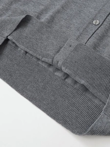 Detail of grey knitted cardigan showing fine ribbed hem and matching round button