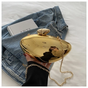 Close-up of gold mango-shaped acrylic clutch bag with metal chain on denim background