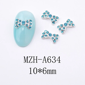 Détail d'un bijou d'ongle en métal argenté en forme de nœud avec strass bleus et dimensions
