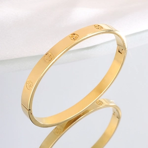 Close-up of gold-plated stainless steel bangle with engraved starburst patterns on silk